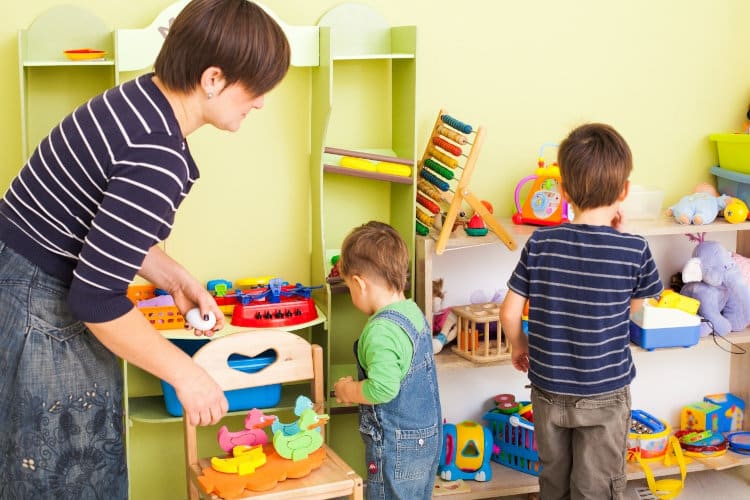 Erzieherin und Kleinkinder räumen gemeinsam auf.